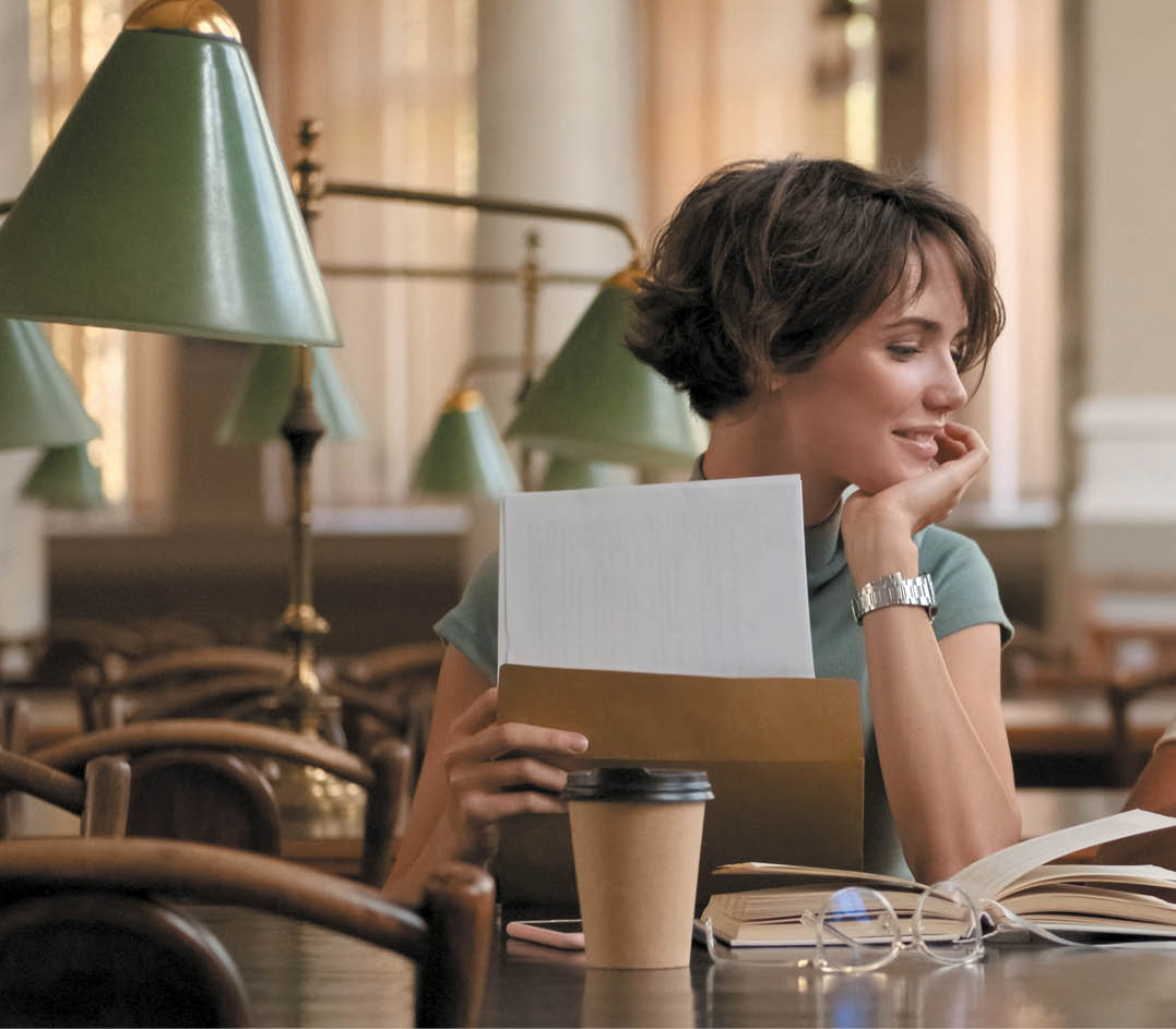 Attractive smiling students happily opening exam results in library  Young casual students studying together in college campus