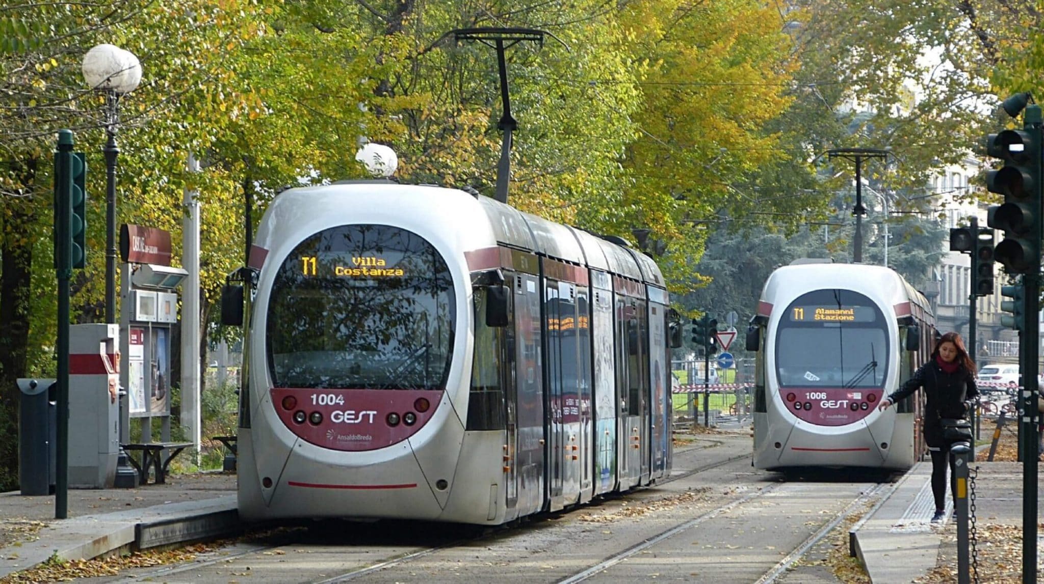 Two trams travelling down street with woman on the right hand side
