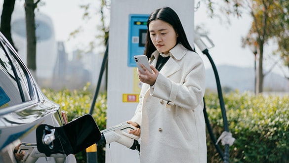 Woman looking at her smart phone whilst charging her electric car